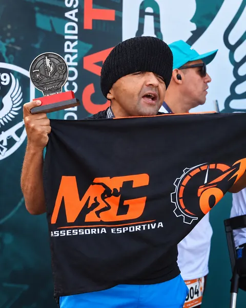 Atleta segurando a bandeira da MG e um troféu