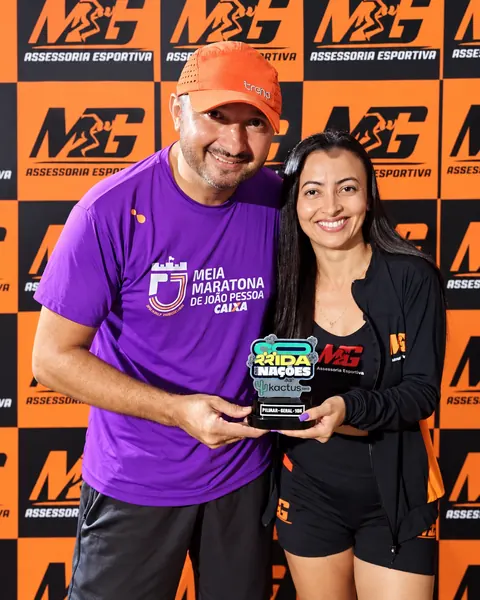 Atletas com troféu em frente ao painel laranja da MG